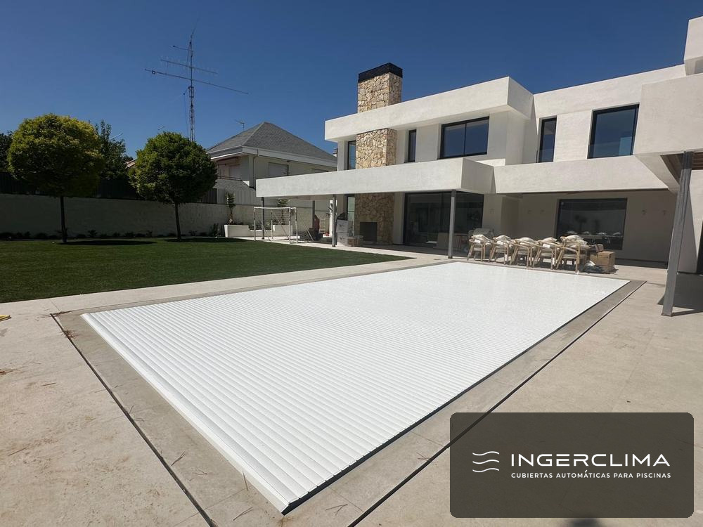 Cubierta de lamas blancas cerrada sobre la piscina de un chalet con césped y seto
