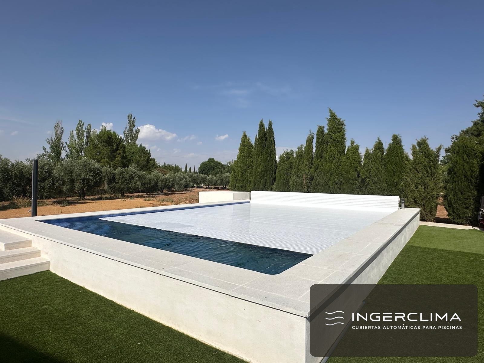 Cubierta automática de lamas blancas cerrada sobre una piscina de jardín, entre olivos y cipreses