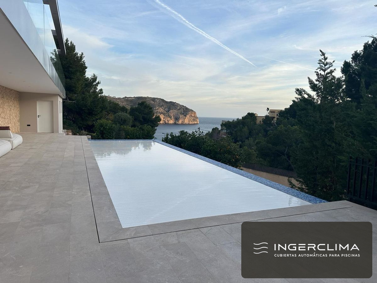 Cubierta de lamas blancas cerrada sobre una piscina desbordante con vistas al mar