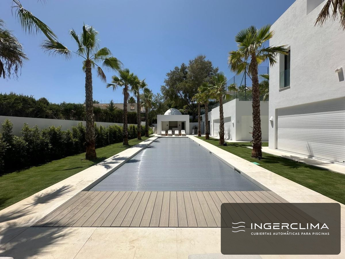 Cubierta automática de lamas grises cerrada sobre la piscina de una villa con palmeras en la Costa del Sol