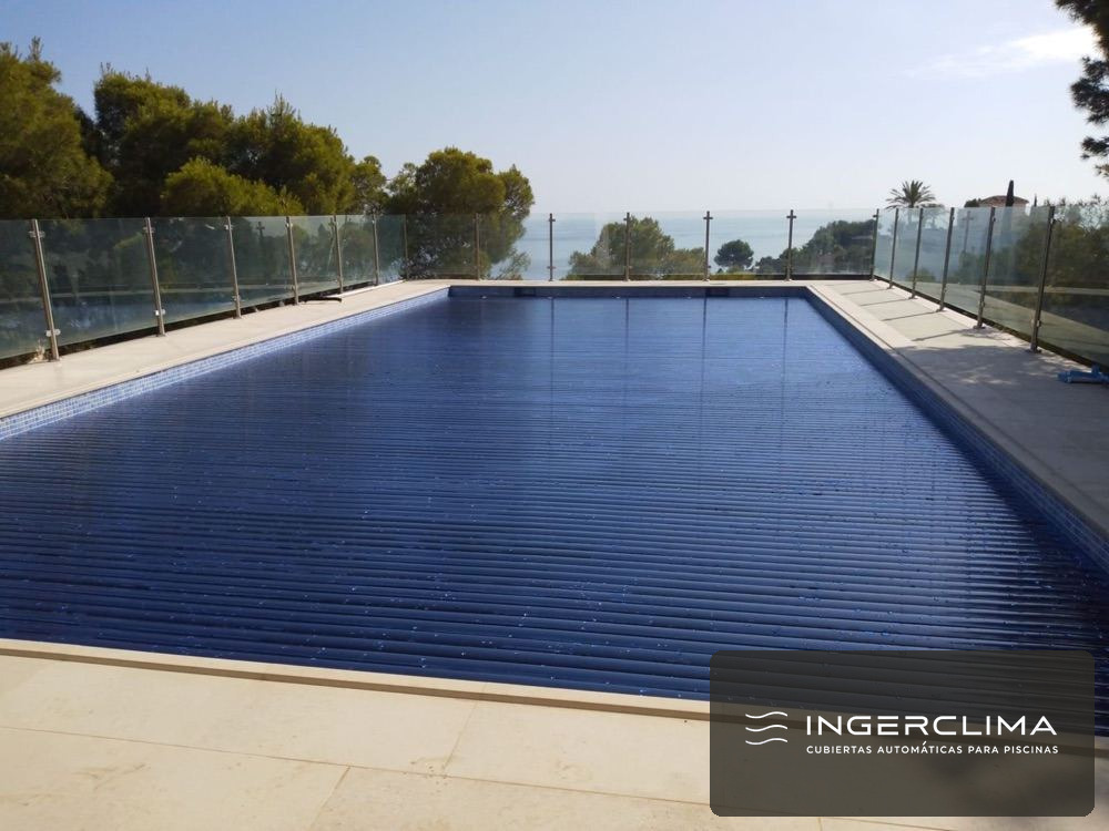 Cubierta automática de lamas sobre piscina rectangular, con el enrollador apoyado en la piedra de coronación