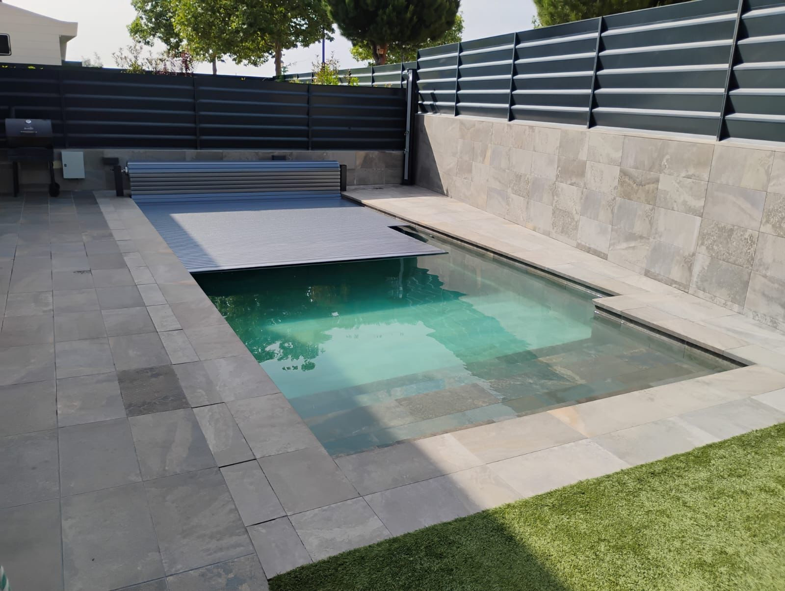 Cubierta automática de lamas grises semiabierta sobre la piscina de un chalet en Granada