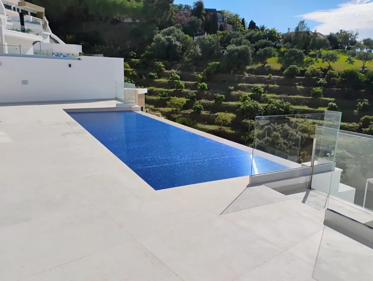 Cubierta automática de piscina con lama de policarbonato solar azul cerrada en una villa a media ladera con vistas al valle en La Herradura, Granada, instalada por Ingerclima junto a Mar Delux