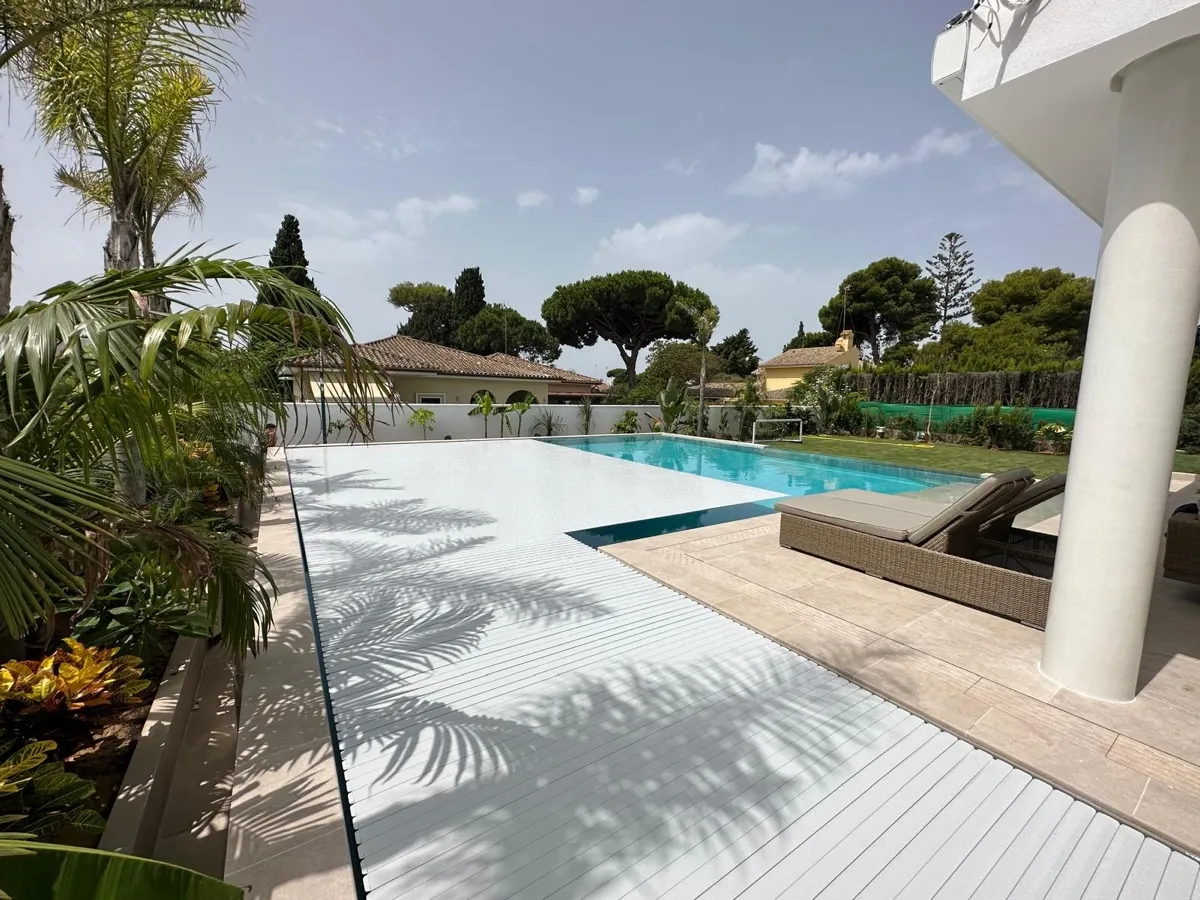 Cubierta automática de lamas de PVC gris cerrada, a ras del pavimento, en una villa de El Puerto de Santa María, Cádiz, instalada por Ingerclima junto a Proyecta Construcción