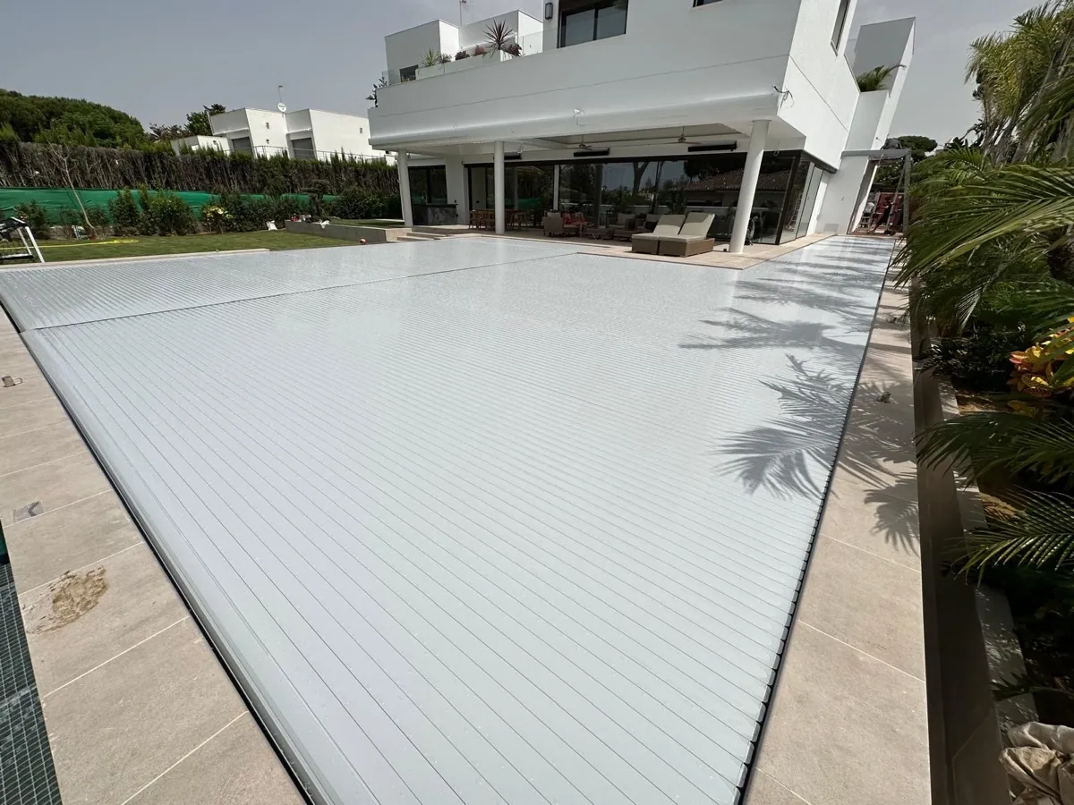 Piscina rectangular cubierta con lama de PVC gris frente a una villa moderna en El Puerto de Santa María, Cádiz, instalada por Ingerclima junto a Proyecta Construcción