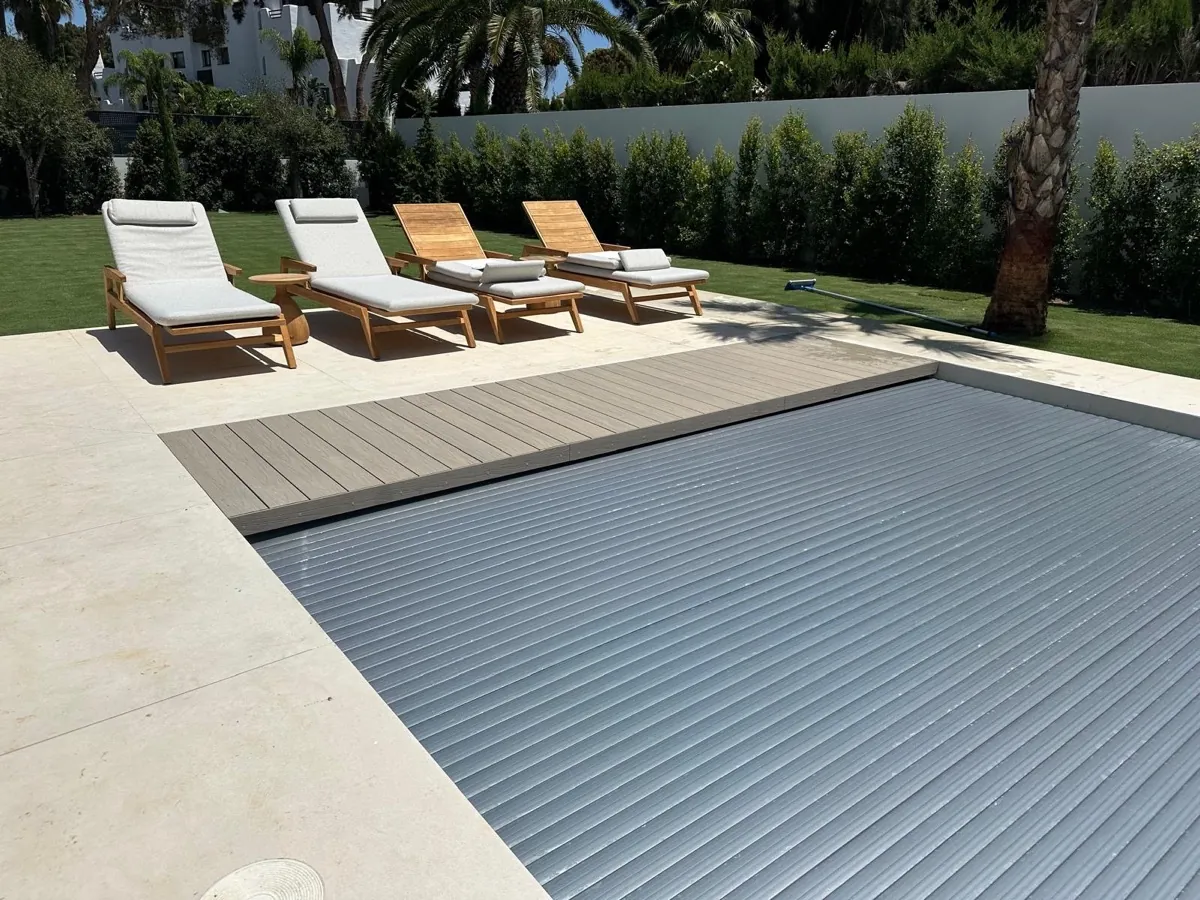 Cubierta automática de piscina con lama de policarbonato solar acabado platinum cerrada, junto a tumbonas de teca, en una villa de Sotogrande, Cádiz, instalada por Ingerclima